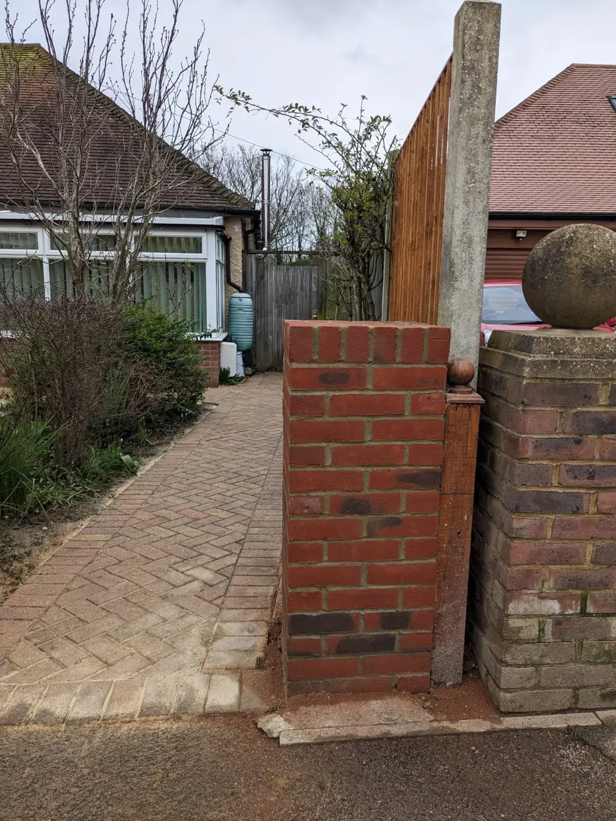 Newly installed red brick pillar adjacent to a block-paved pathway at a home entrance.