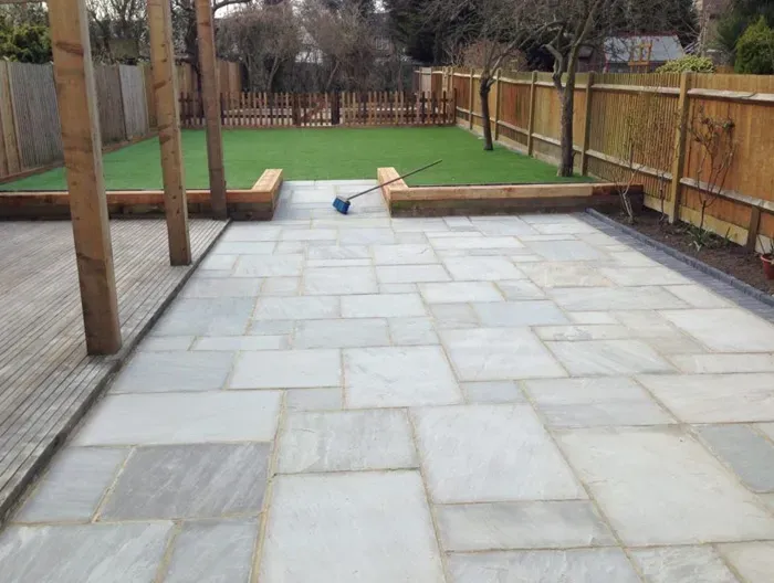 A contemporary garden design showcasing a spacious natural stone patio, adjacent decking, artificial grass, and new fencing by Elite Paving and Roofing LTD.