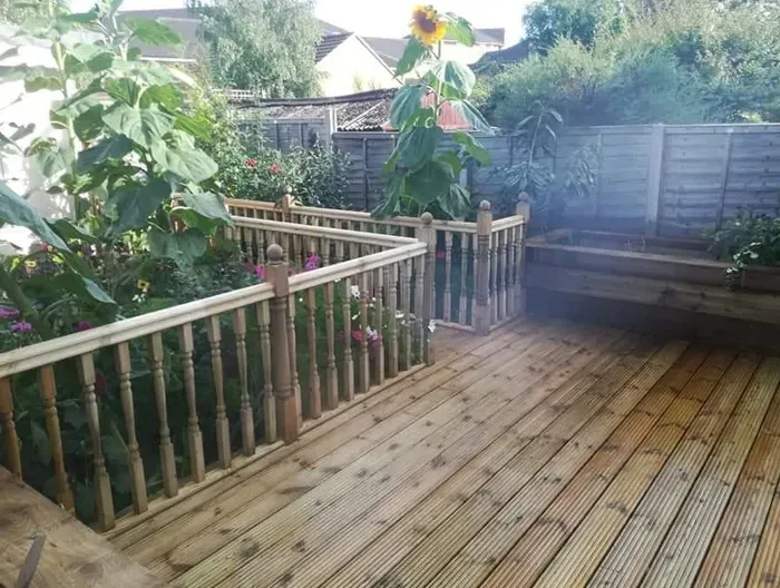 Wooden garden deck with railings and a vibrant garden.