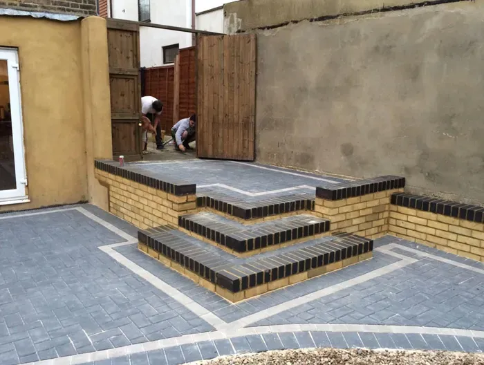 Newly laid block paving patio with intricate brick steps and a contrasting border design, showcasing professional landscaping work in progress.