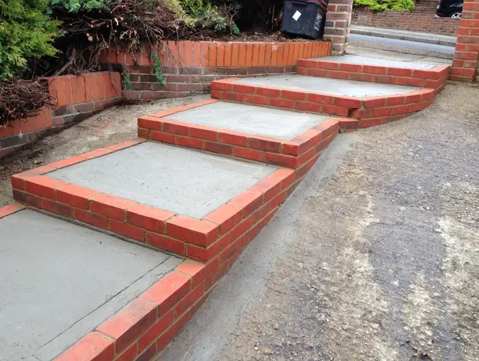 Close-up of newly built red brick steps with grey concrete surfaces and a matching brick garden wall in a residential outdoor area.