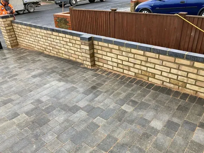 A close-up of a newly installed block paved driveway and a matching brick garden wall with dark coping, demonstrating professional hard landscaping services.