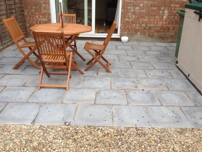 A modern grey slab patio with wooden garden furniture and a gravel border.