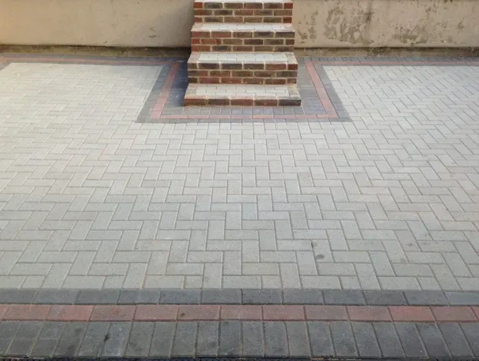 Newly laid light grey block paved driveway or patio with dark border and brick steps