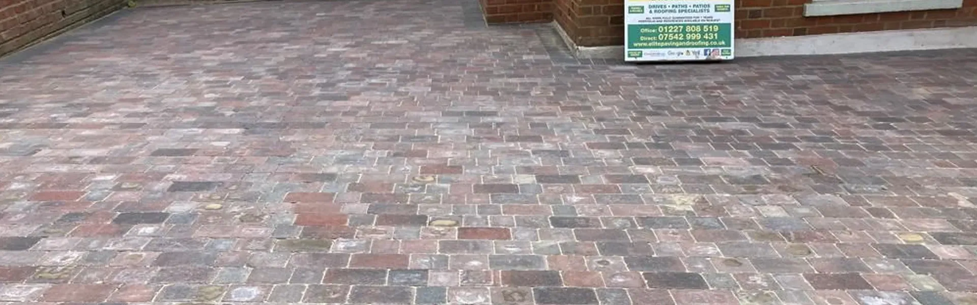 A multi-coloured block paving driveway leading to a residential home, with an Elite Paving and Roofing LTD sign visible on the right.