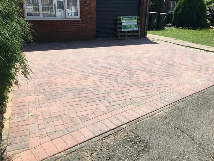 A freshly laid block paved driveway in red and grey, featuring a herringbone pattern and a clean border, leading to a garage.