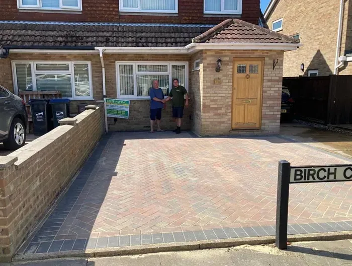 Newly completed block paved driveway with a herringbone pattern in front of a house, two men shaking hands by an Elite Paving sign, and a 'Birch C' street sign.