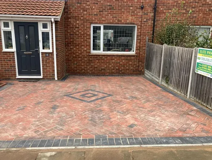 A new block-paved driveway featuring a herringbone pattern and a central diamond design, in front of a modern brick house.