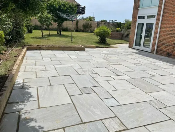New grey natural stone patio in a garden with a lawn and house in the background.