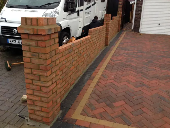 A new block paved driveway in a herringbone pattern with a recently constructed brick wall and pillars.